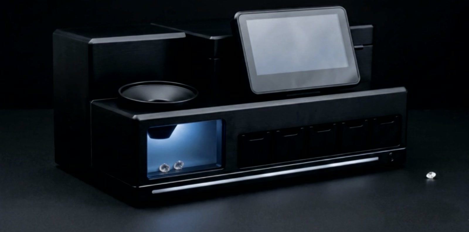 The desk grading machine: a feed hopper, a touchscreen, a lit scanning chamber with stones inside, and a row of sorting bins along the front.