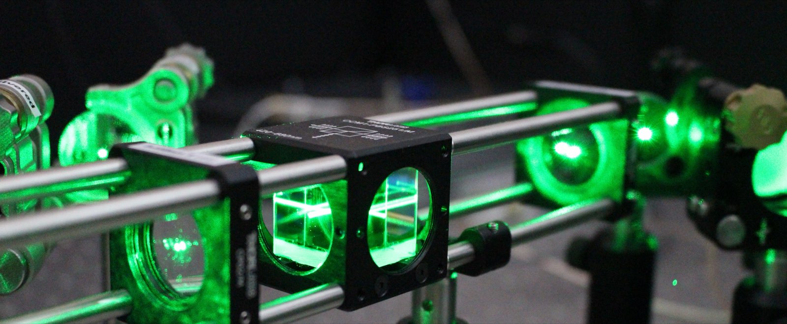 A green 532 nanometre laser passing through beamsplitter cubes on an optical bench in a quantum sensing laboratory.